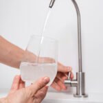 Woman get filtered water from stainless faucet into a glass.